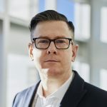 Profile portrait of a confident business executive wearing eyeglasses in a sunlit office setting.
