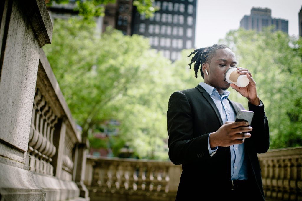 Young professional enjoying coffee while using smartphone in urban park.