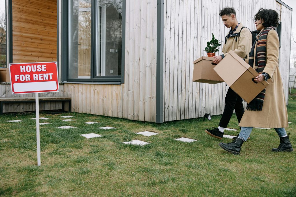 Young couple carrying boxes into their newly rented house, symbolizing new beginnings.